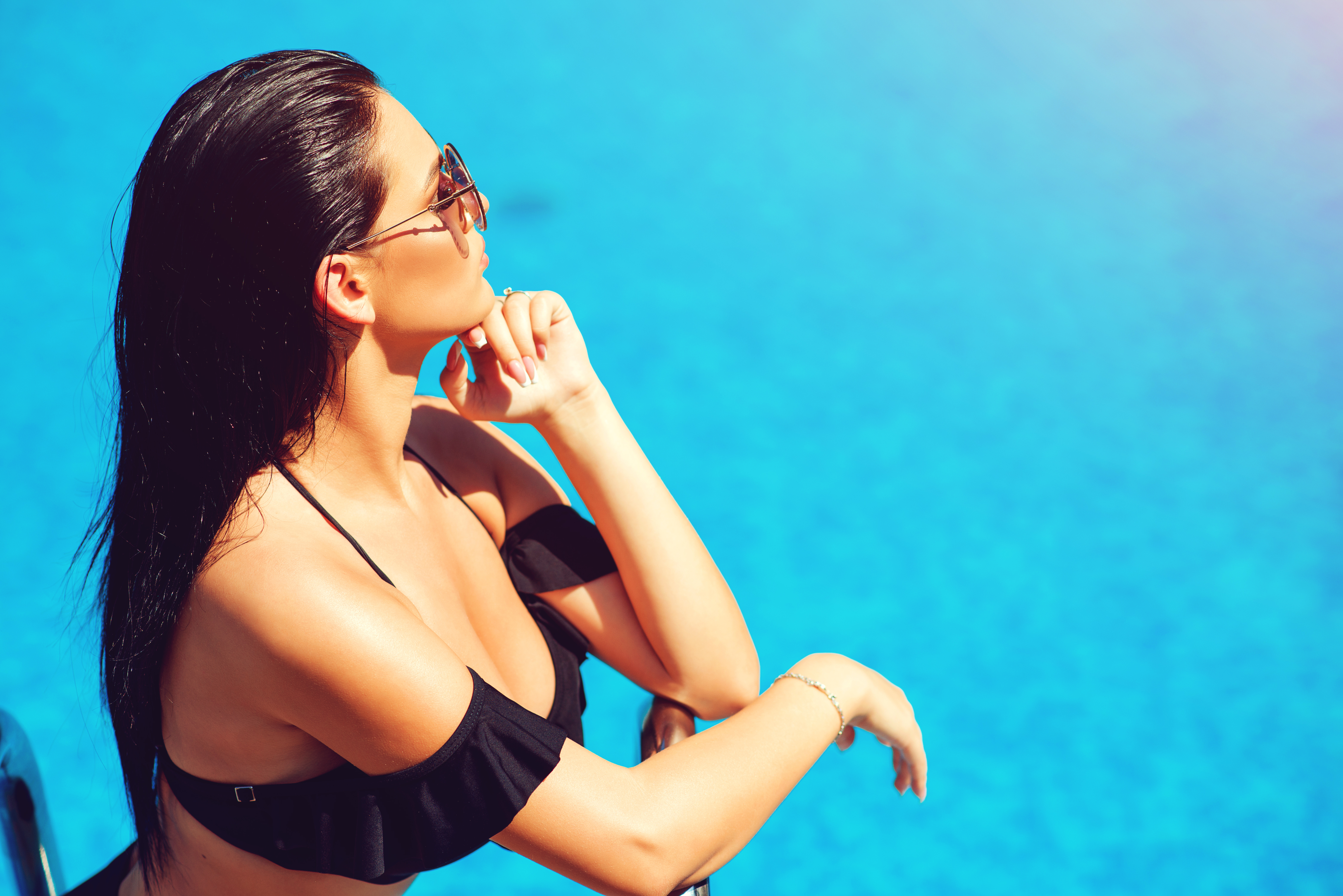 Woman posing in pool as she protects her skin and eyes with sunscreen and sunglasses.